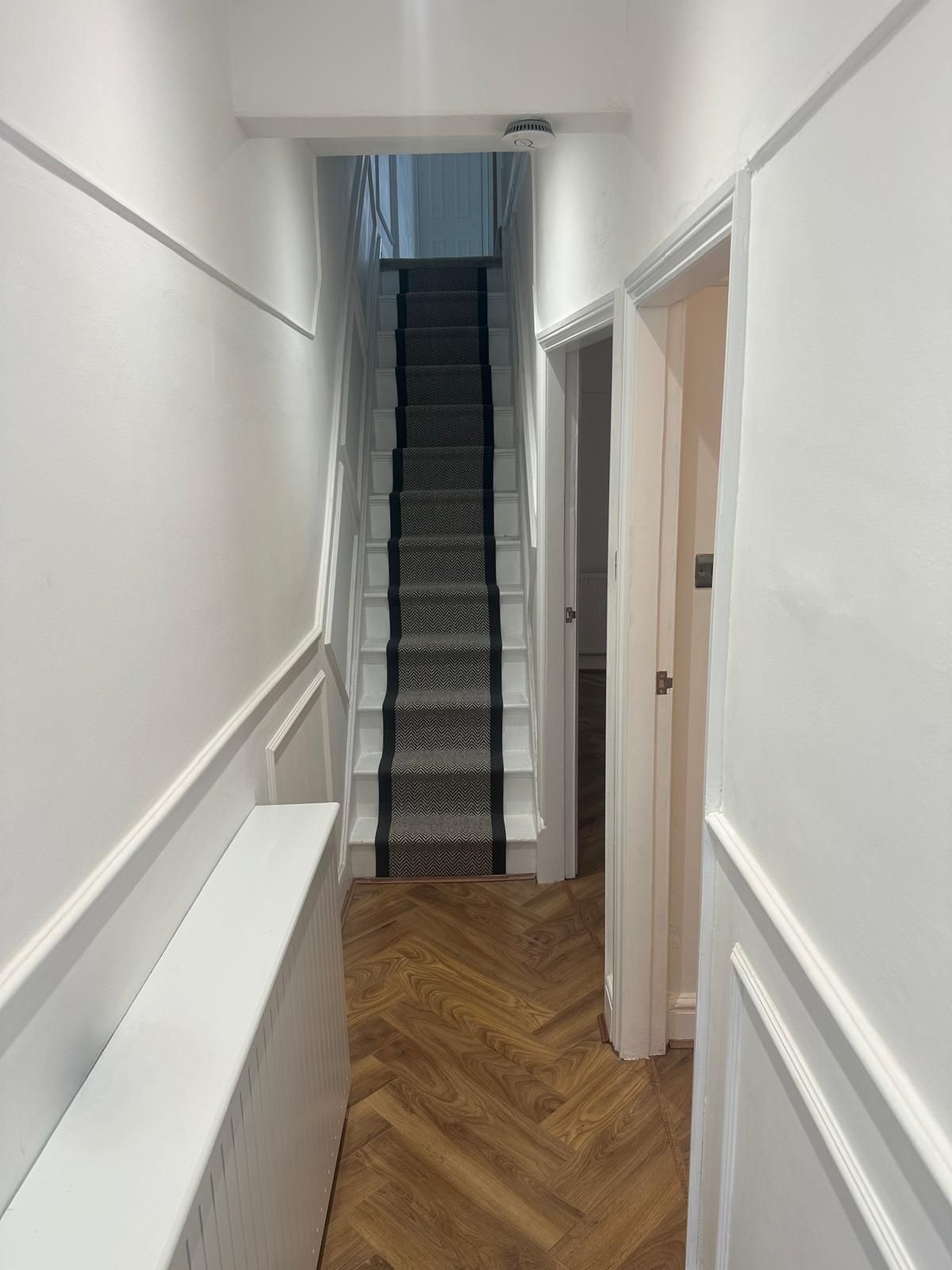 White panelled hallway with herringbone floor and black-edged stair runner